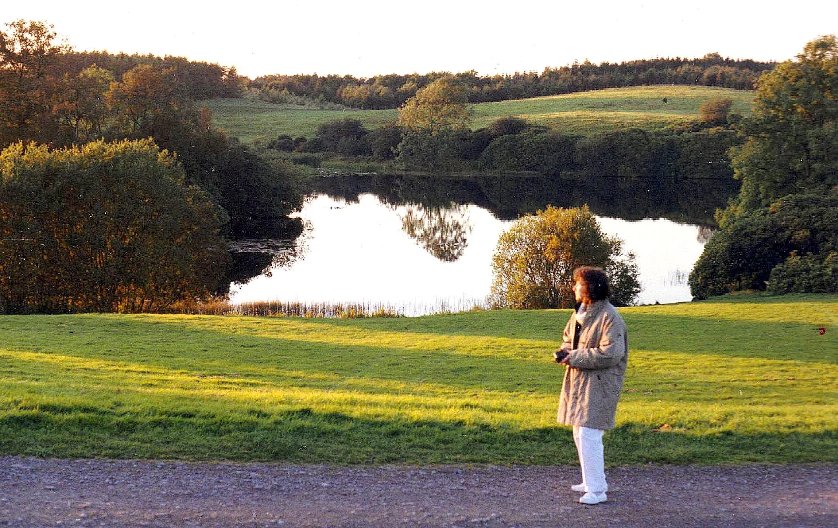 Castle Lake at Rossmore Forest Park, still water with wooded drumlin slopes running down to the far shore.